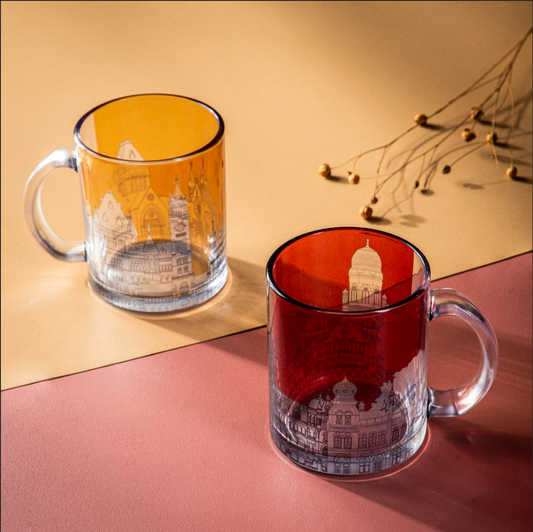 Two clear glass mugs with red and yellow coloring, featuring gothic architectural designs, placed on a surface with a reflection and a subtle background.